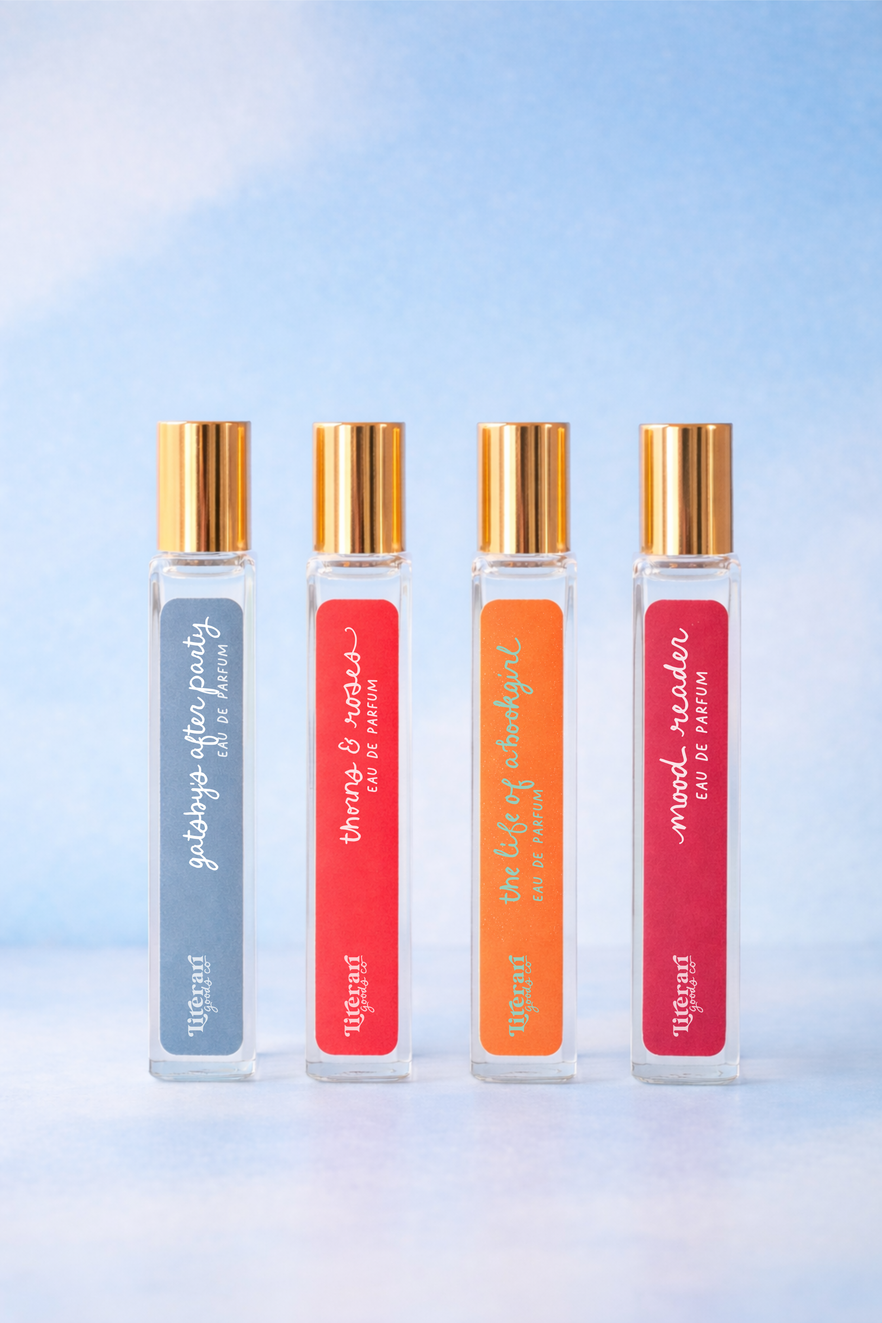 Four book themed roll on perfume bottles with gold caps on a gradient blue background